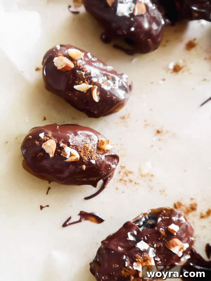 Autumn Spiced Chocolate Pumpkin Dates 10 Chocolate covered pumpkin stuffed dates sprinkled with sea salt, crushed almonds, and pumpkin spice, arranged on parchment paper.