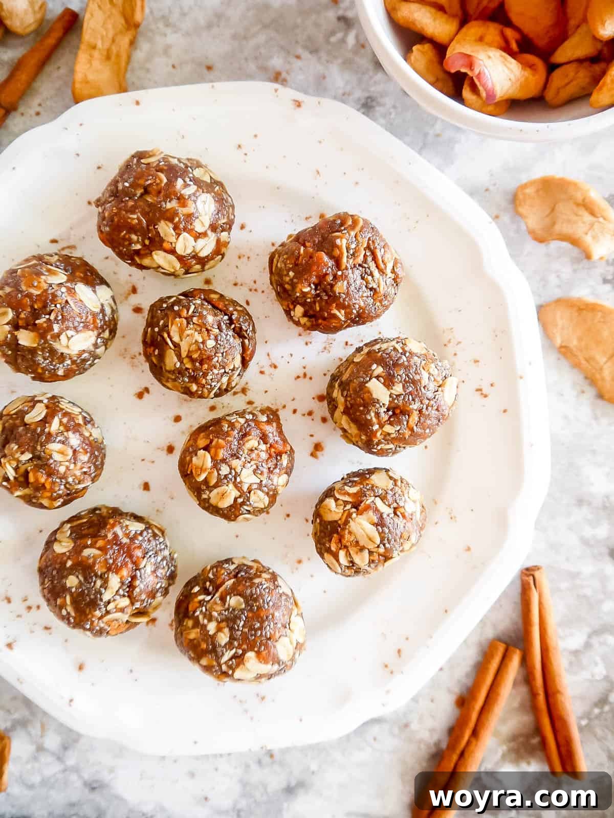 A stunning arrangement of apple pie energy balls, some dusted with cinnamon, on a white plate, ready to be enjoyed.