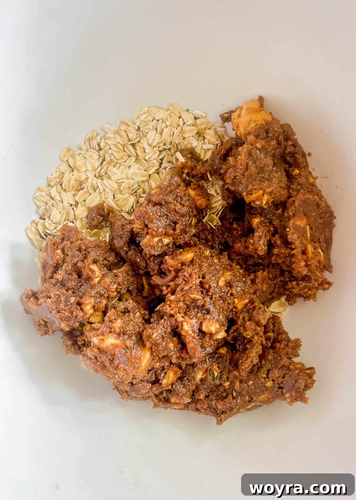 The processed date mixture is poured over the rolled oats and chia seeds in a bowl.