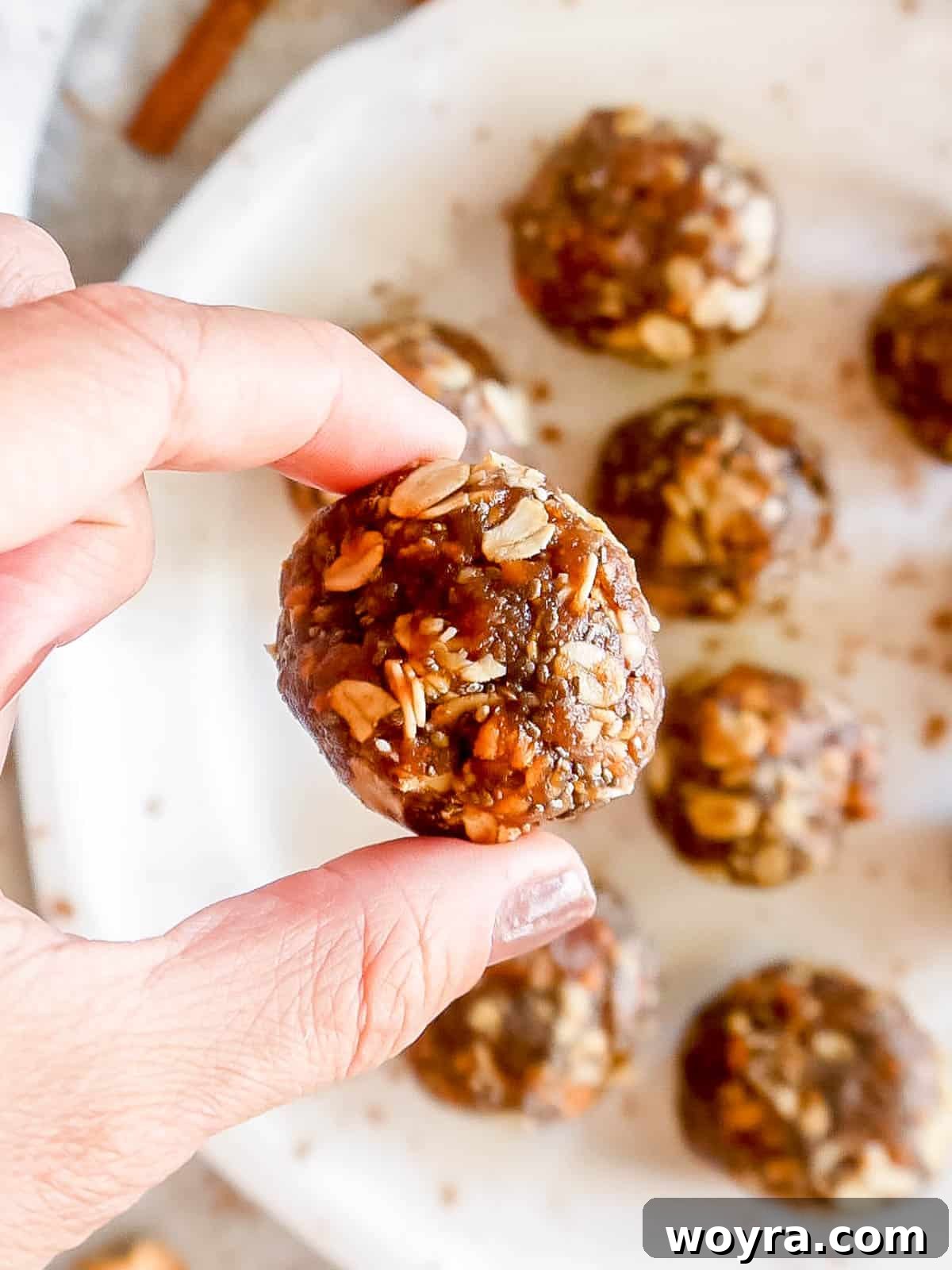 A hand is shown rolling a portion of the apple cinnamon energy ball dough into a perfect spherical shape.