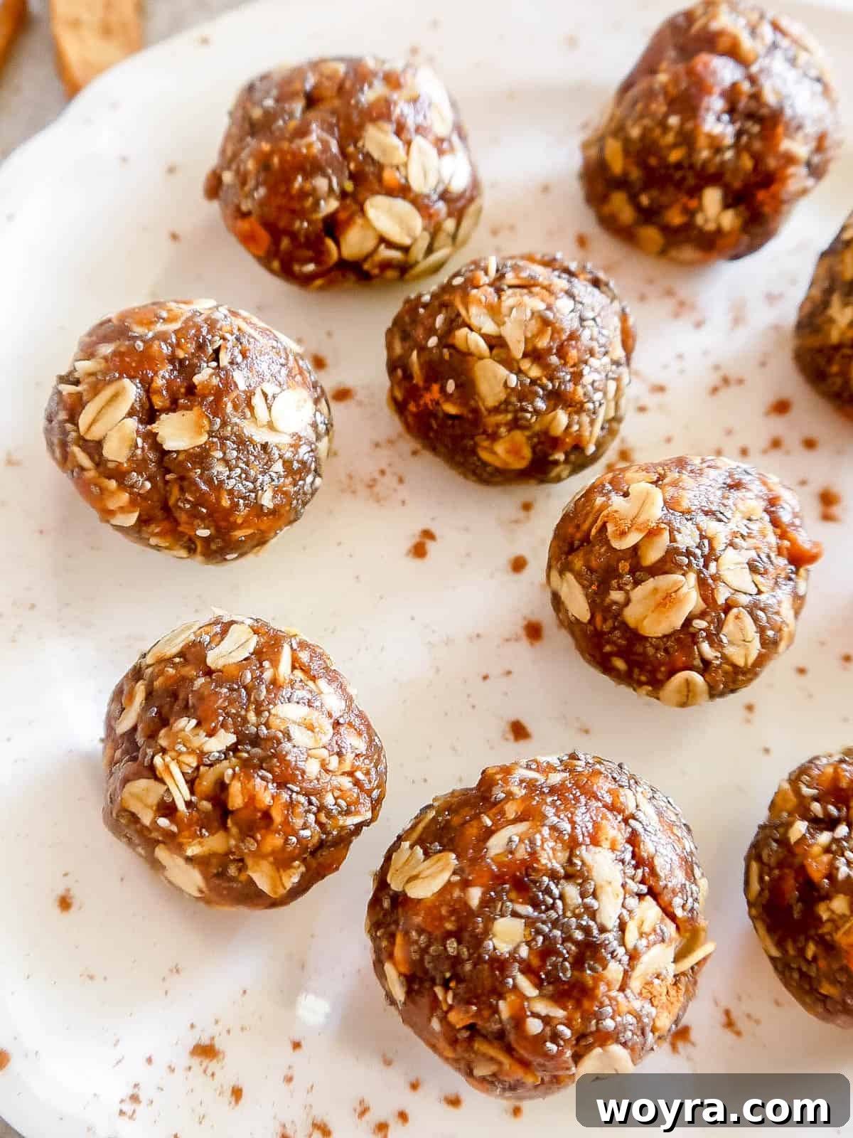 A plate of freshly rolled apple pie energy balls, lightly dusted with cinnamon, ready for chilling.