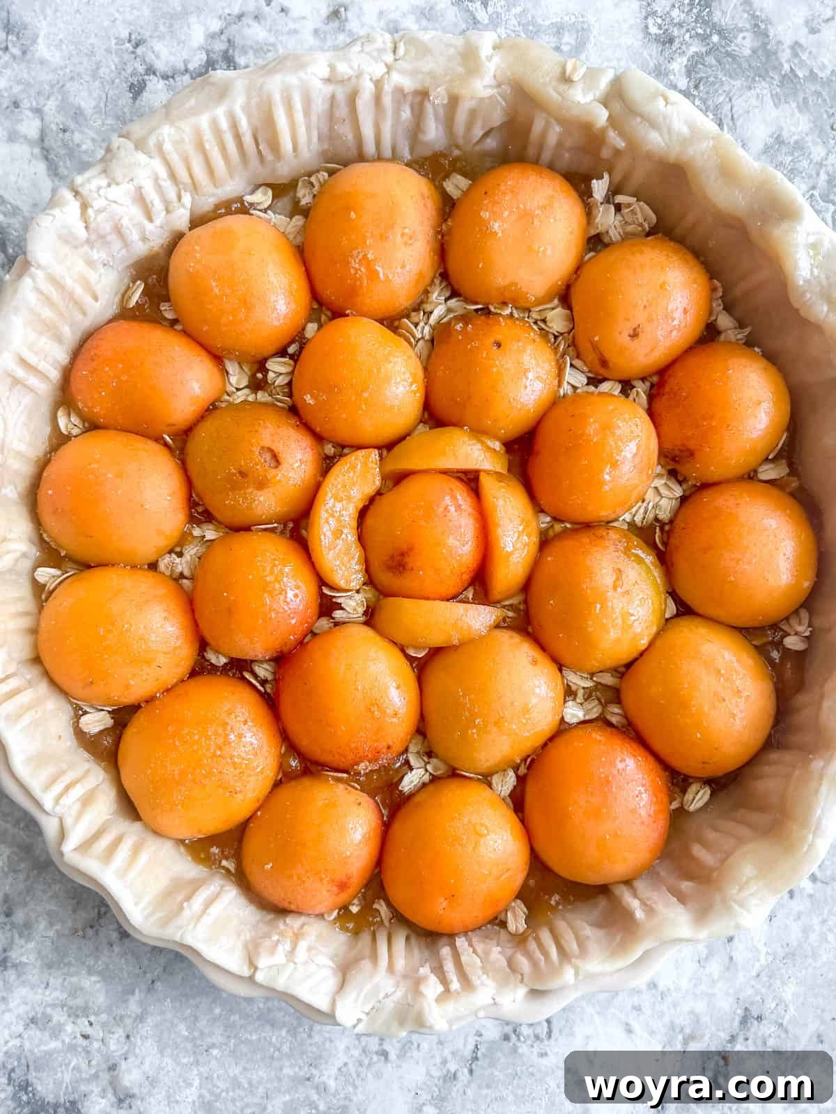 Effortless Apricot Tart 7 Rolled oats sprinkled over jam, followed by halved apricots arranged in a circular pattern, ready for baking.
