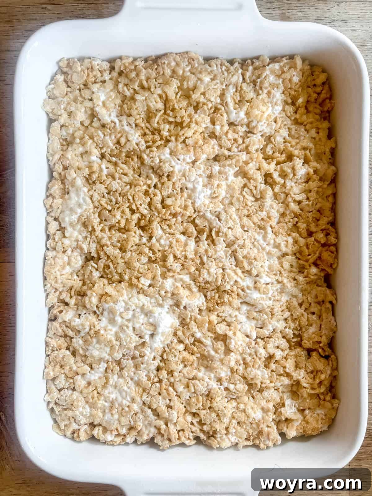 Campfire S'mores Krispie Bars 11 The S'mores Rice Krispie Treat mixture is pressed firmly and evenly into a greased baking pan, creating a smooth layer.