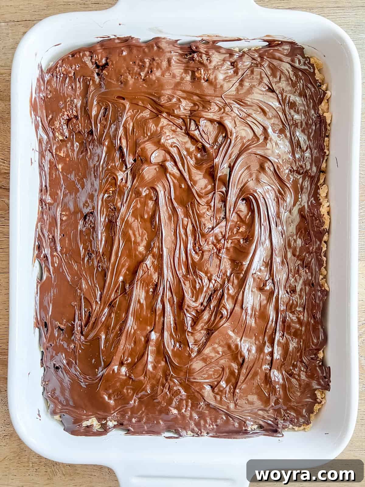 Campfire S'mores Krispie Bars 13 Melted chocolate is being spread smoothly over the top of the S'mores Rice Krispie Treat base in the pan.