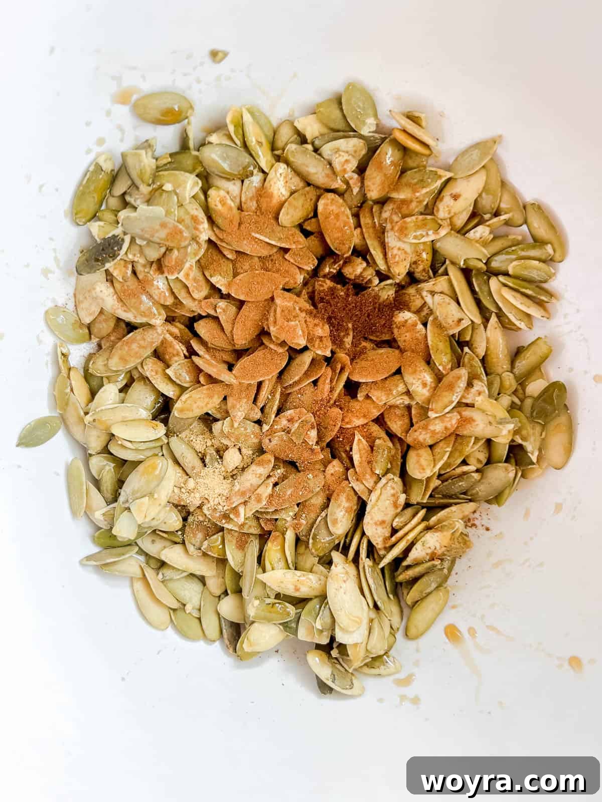 Pepitas in a bowl, coated with maple syrup and spices, being mixed.