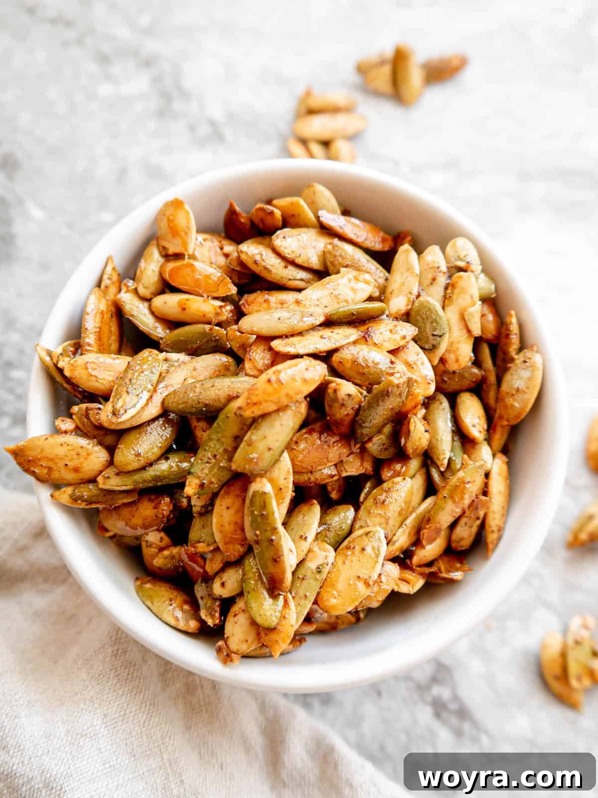 A generous serving of maple roasted pumpkin seeds, perfectly glazed and spiced, presented in a small white bowl.