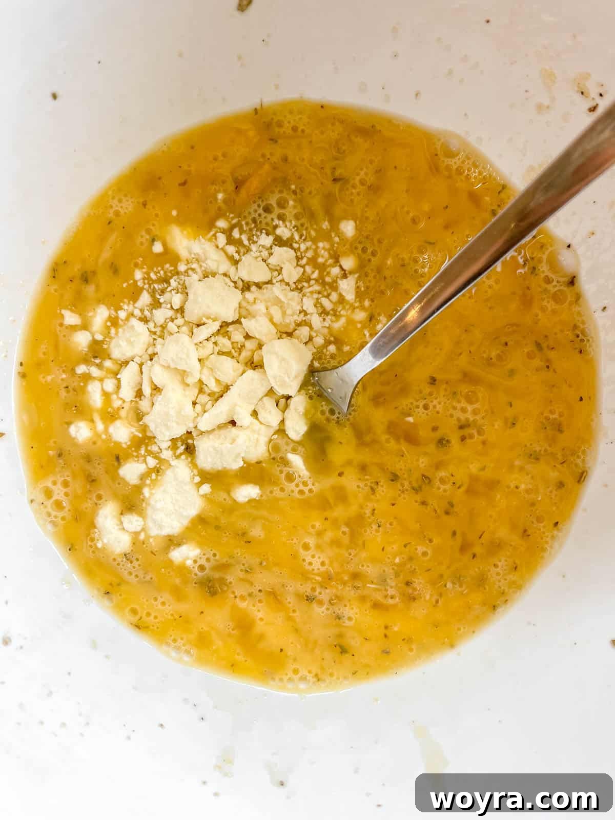 Spinach Feta Egg Bites 6 Feta cheese and dried spices being added to the whisked egg mixture in a bowl.