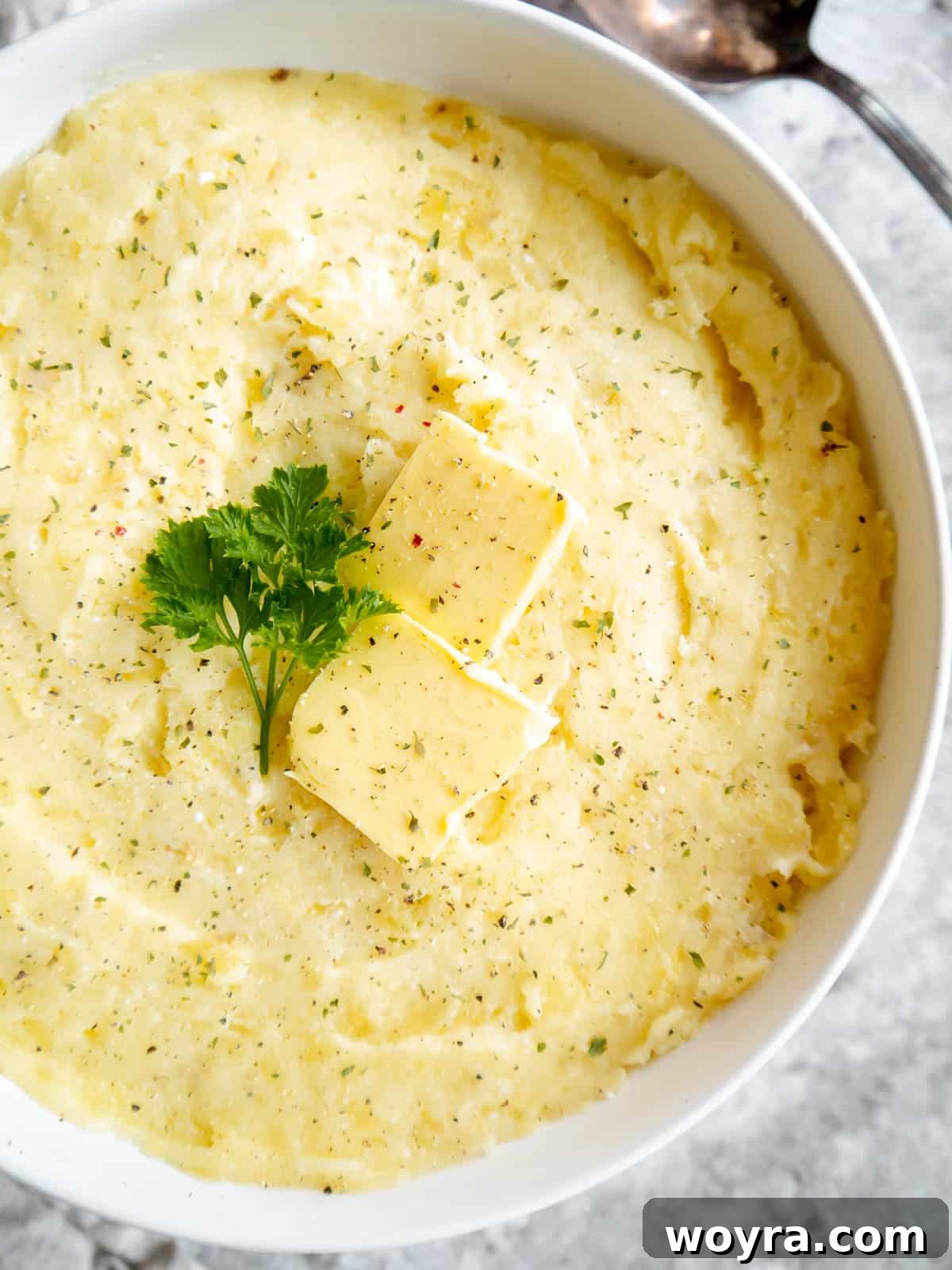 A large bowl of creamy cottage cheese mashed potatoes with a dollop of butter melting on top, garnished with fresh herbs.