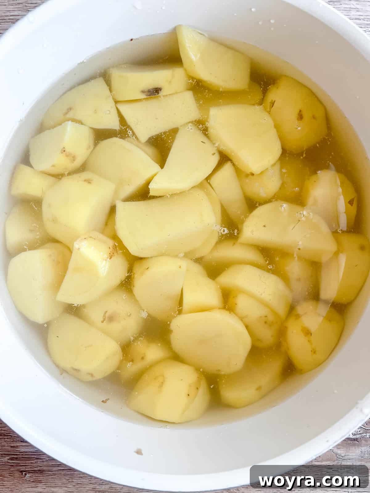 Sliced potatoes boiling in a large pot of hot water on the stove.