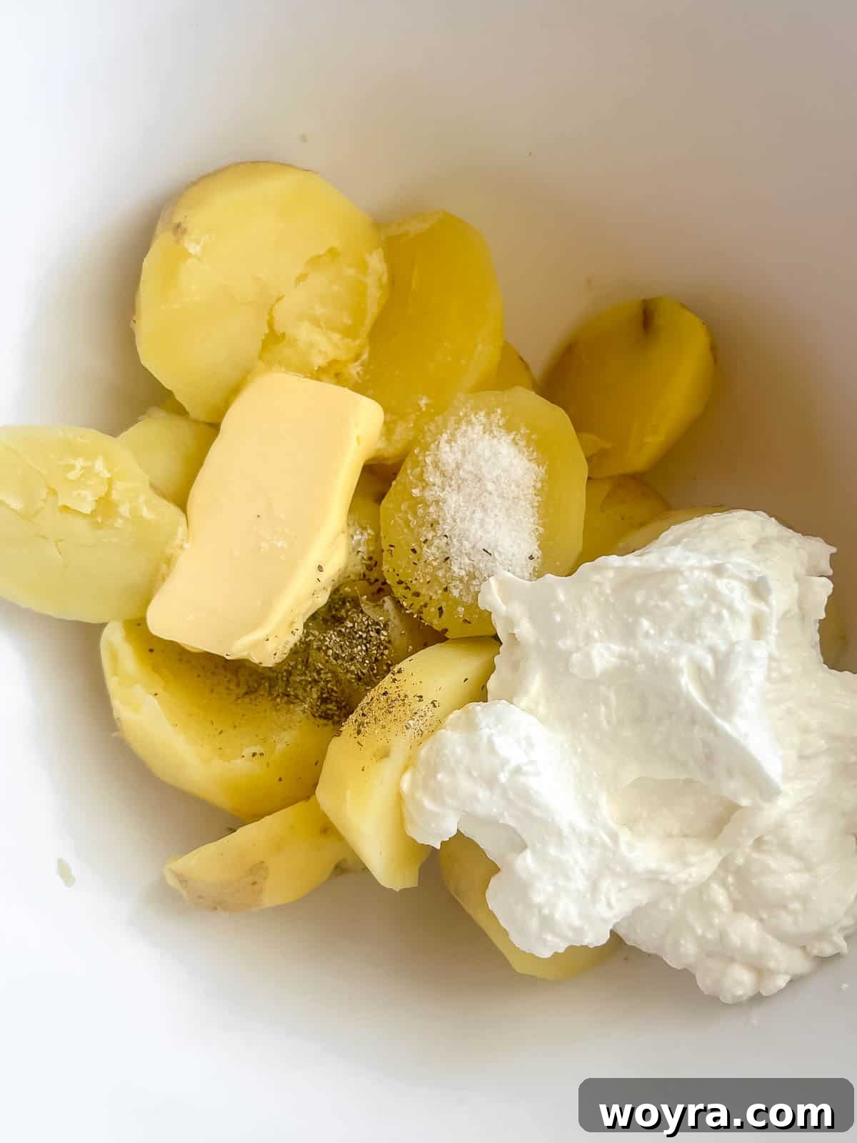 Hot boiled potatoes, whipped cottage cheese, butter, salt, and pepper in a large mixing bowl, ready to be mashed.