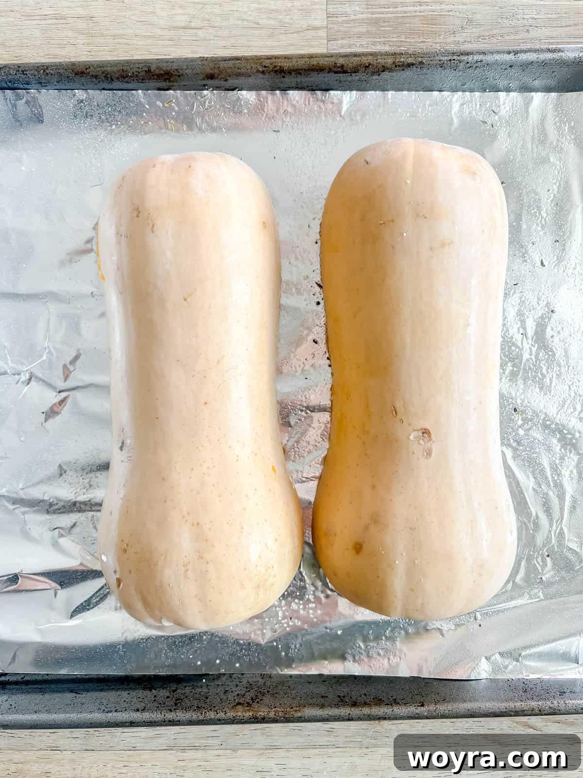Butternut squash halves placed cut side down on a baking pan.