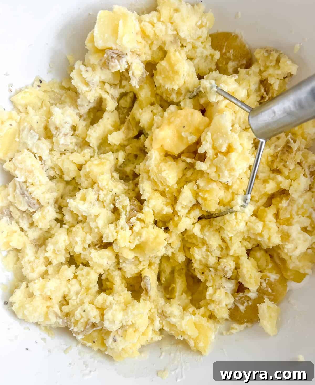 Mashing Greek yogurt mashed potatoes in a bowl with a potato masher.