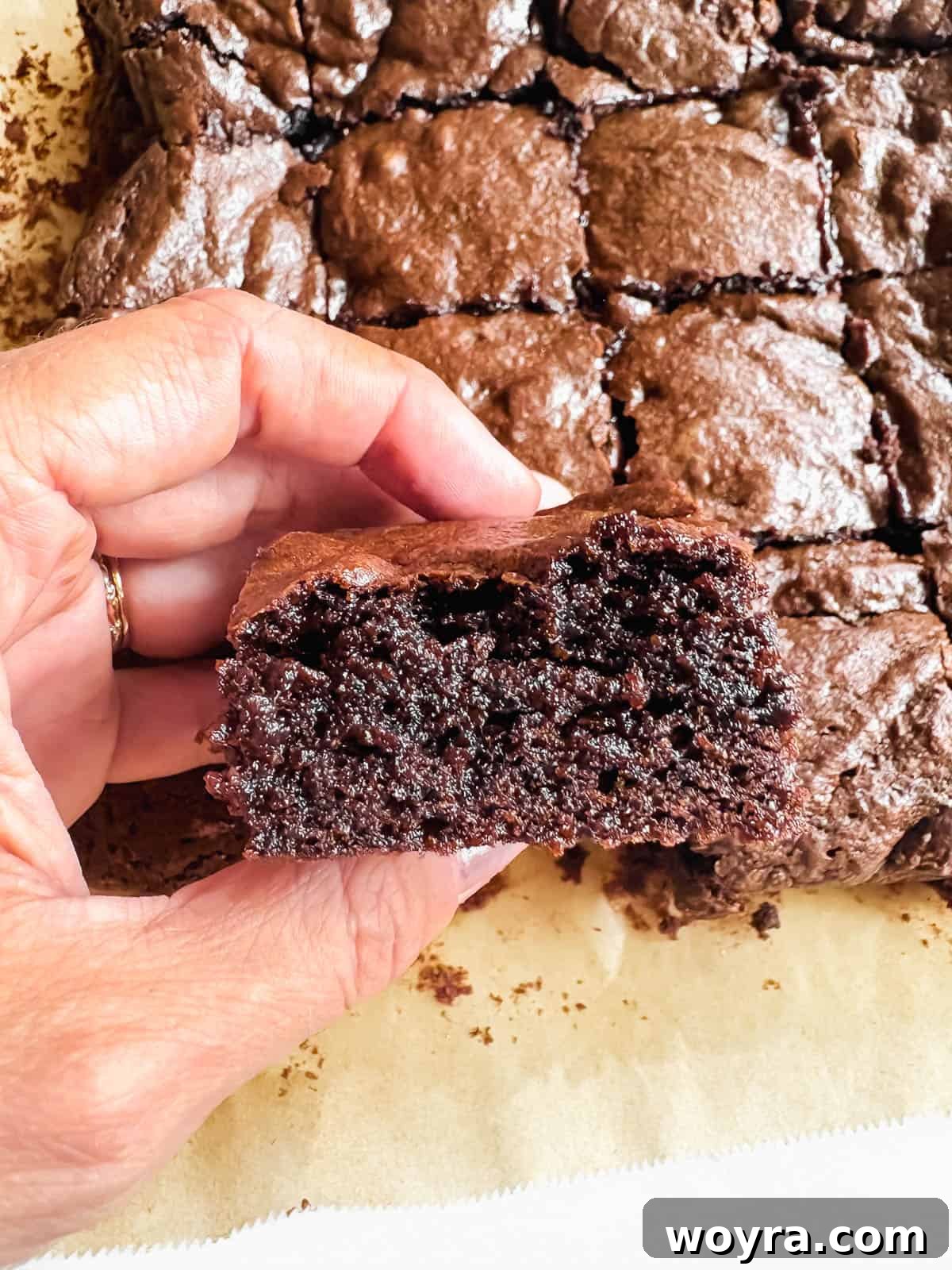 Silky Olive Brownies 12 A hand gently holds a perfectly cut, rich olive oil brownie square, showcasing its dense, glossy top and incredibly fudgy interior.