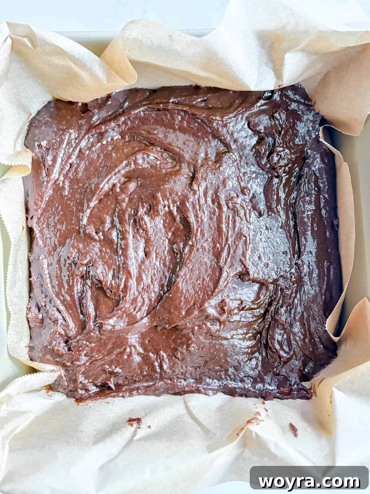 Silky Olive Brownies 9 The rich olive oil brownie batter, perfectly spread and leveled in a parchment-lined 8x8 inch baking pan, poised for the oven.