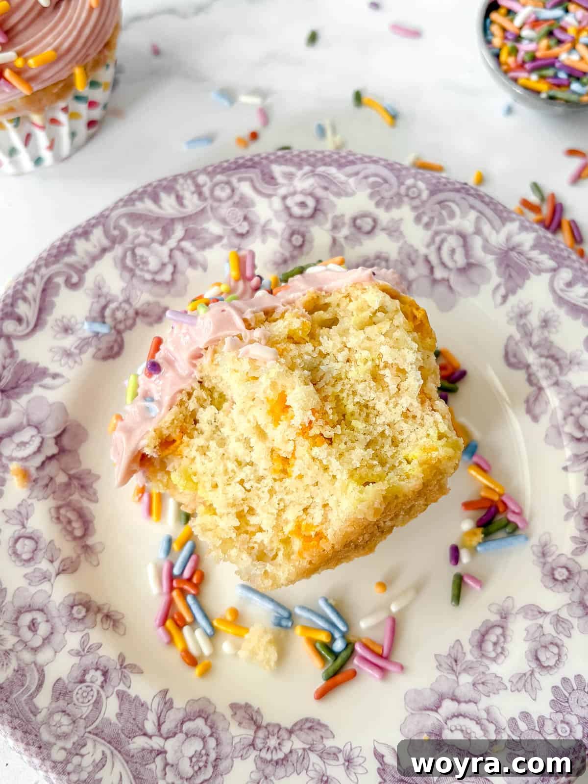 Whimsical Small Batch Funfetti Cupcakes 13 A homemade funfetti cupcake with pink frosting and sprinkles, showing a bite taken out to reveal the colorful inside.