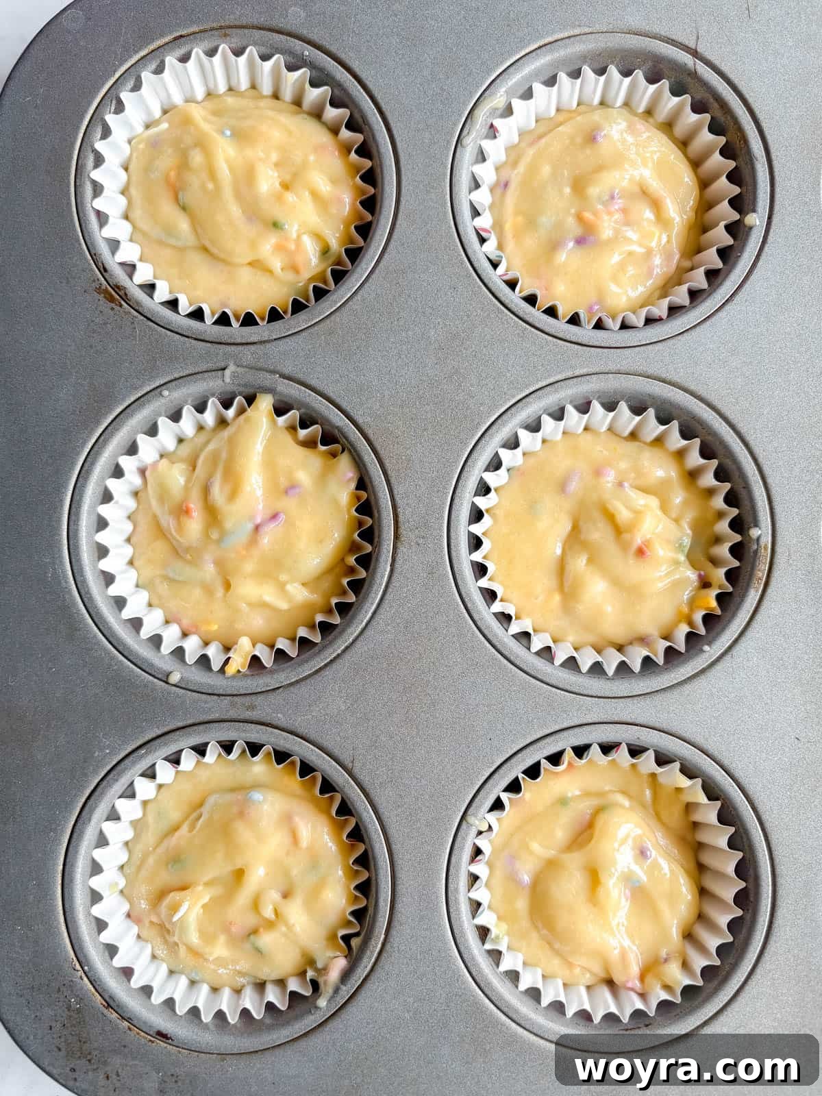 Whimsical Small Batch Funfetti Cupcakes 9 Six cupcake liners in a muffin tin, each filled evenly with funfetti cupcake batter before baking.