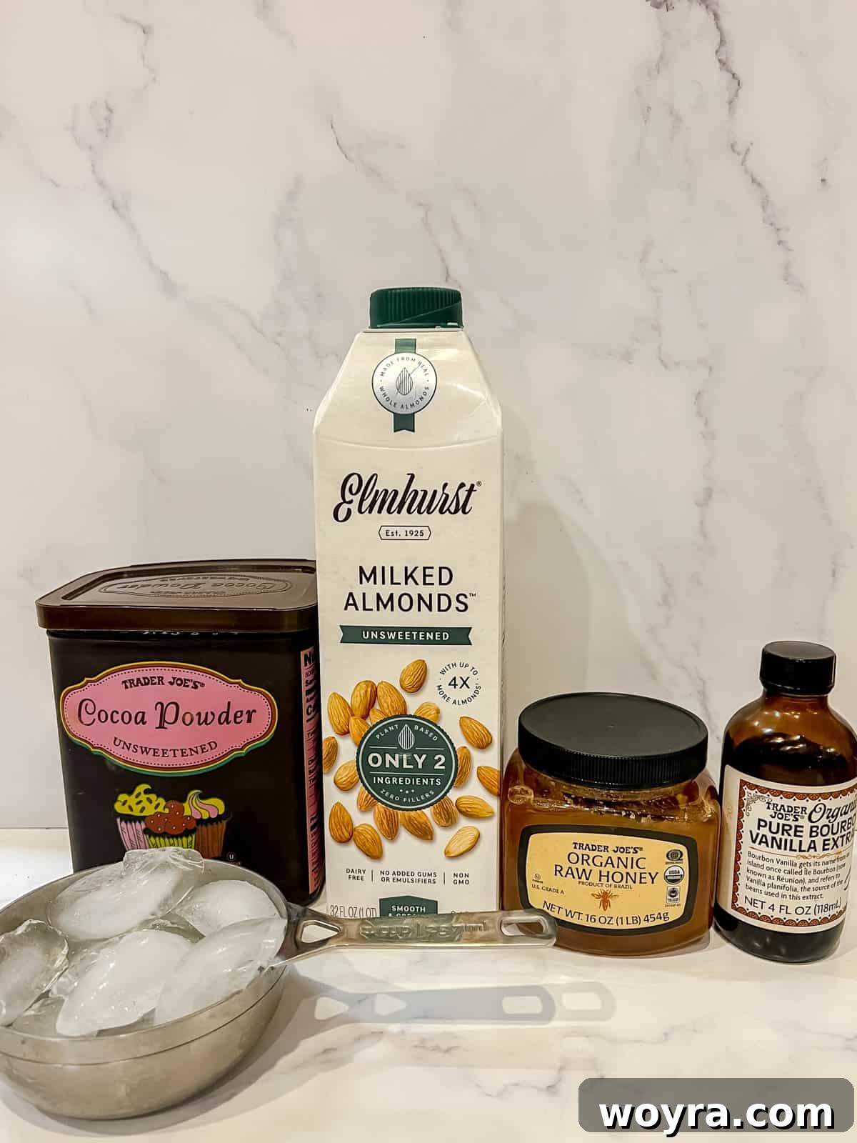 Creamy Paleo Dairy Free Frozen Hot Chocolate 3 Collection of ingredients including honey, cocoa powder, coconut milk, vanilla extract, and ice cubes, ready to make frozen hot chocolate.