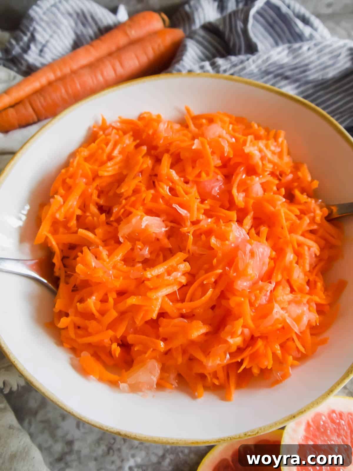 Tangy Citrus Carrot Crunch 5 A large serving bowl filled with a beautiful raw carrot grapefruit salad, accompanied by serving spoons.