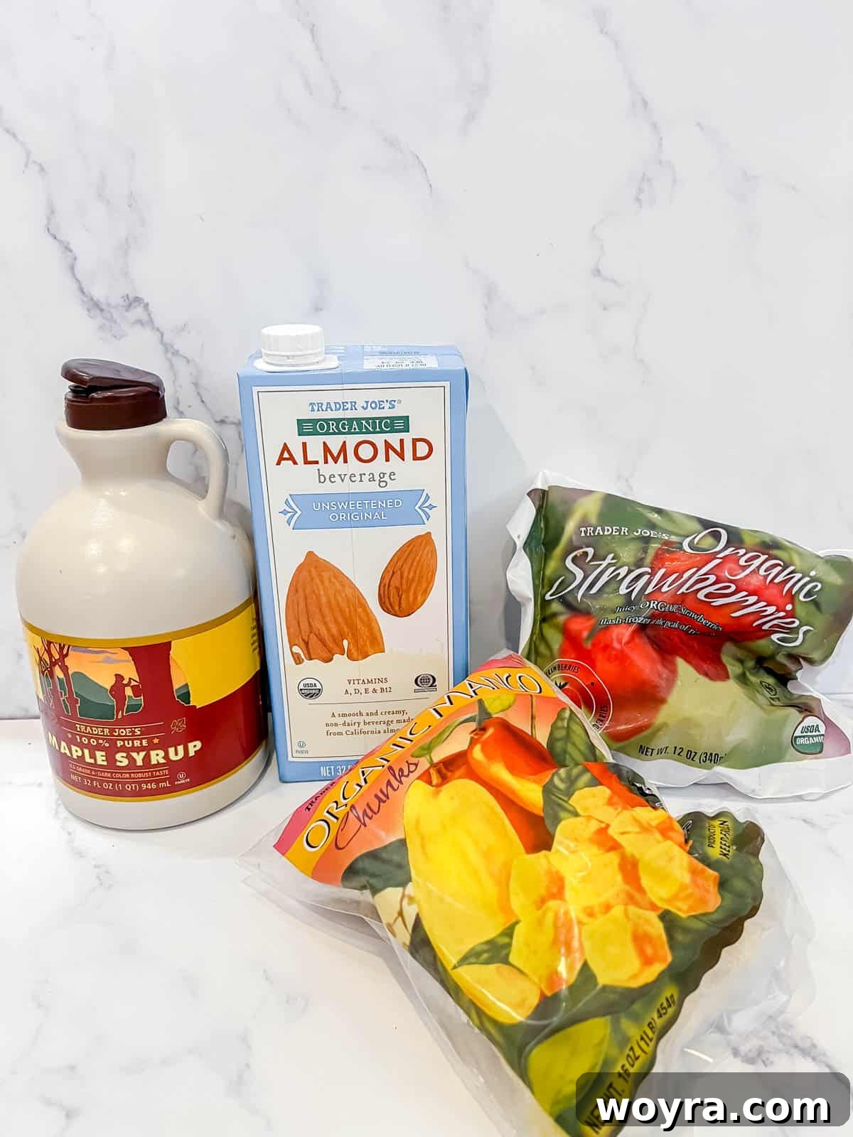 Strawberry Mango Blender Sorbet 3 A flat lay image showing the simple ingredients required for strawberry mango sorbet: frozen strawberries, frozen mango, a carton of milk, and a bottle of maple syrup.