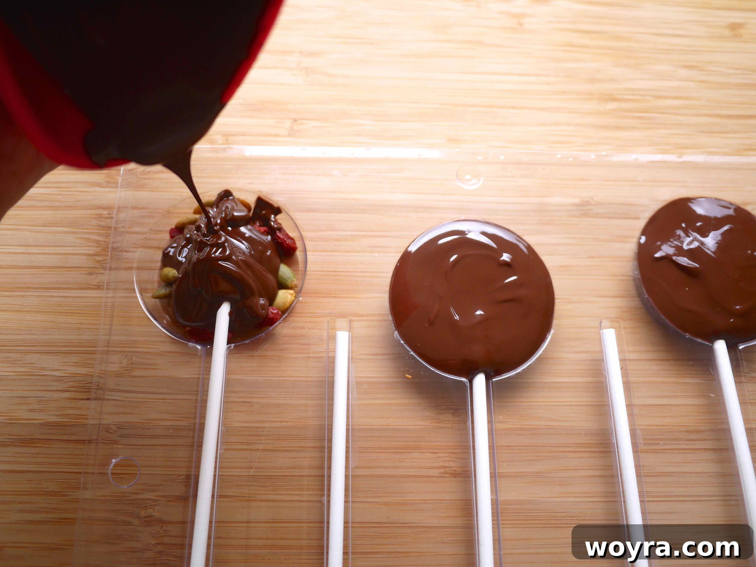 Artisan Chocolate Fruit Pops 5 Smoothly pouring melted chocolate into the lollipop molds, covering the pre-arranged fruits and nuts.