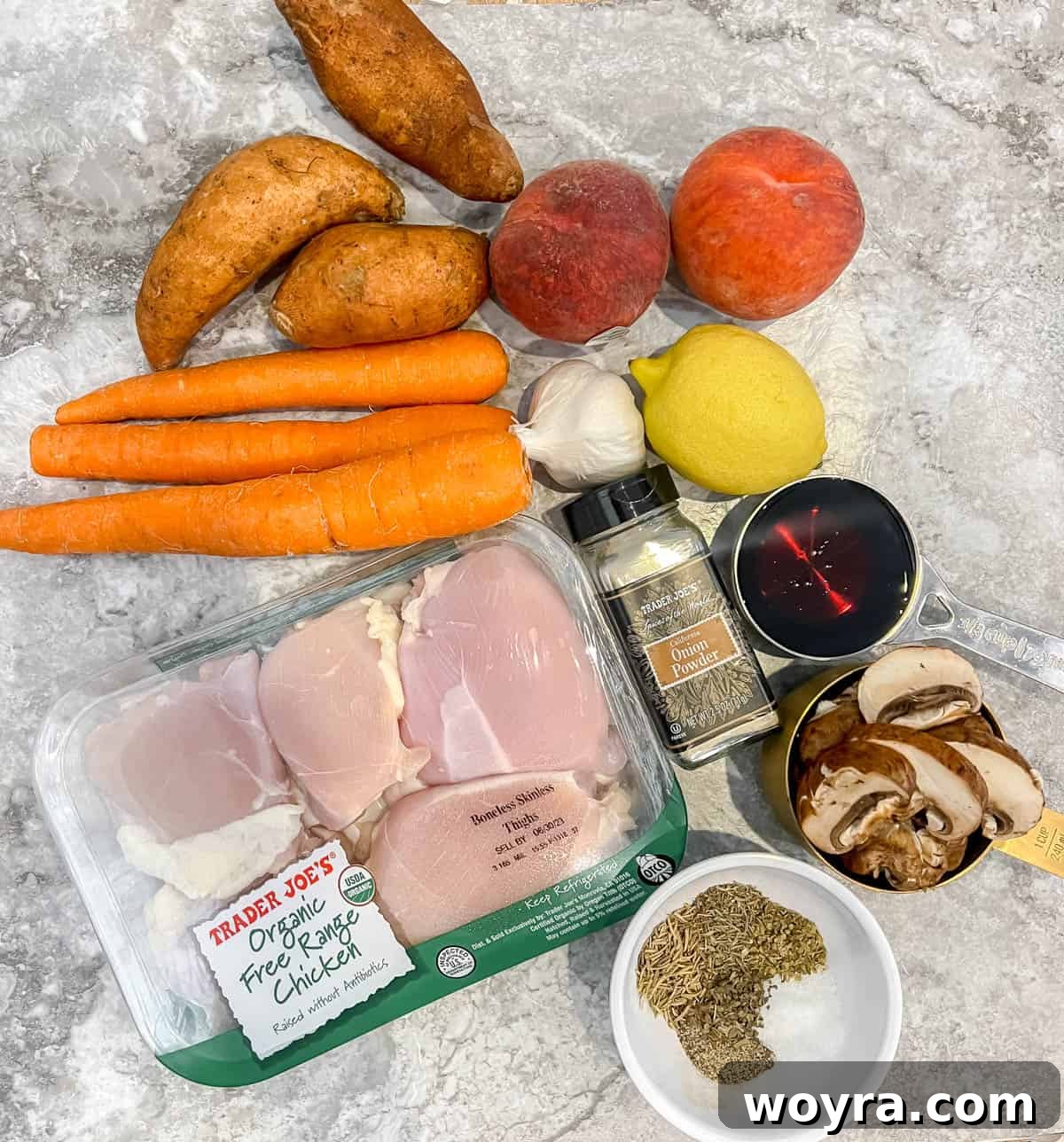 A collection of fresh ingredients laid out, including peaches, chicken, carrots, and herbs, ready for the peach chicken dish.