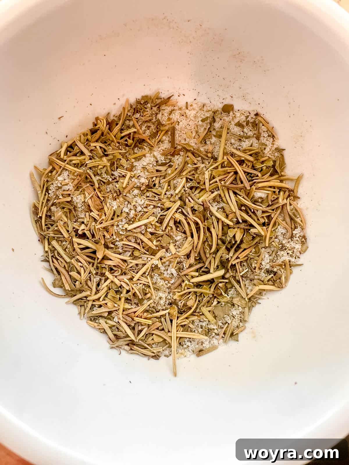 A small bowl containing a mixture of dried herbs and spices for seasoning.