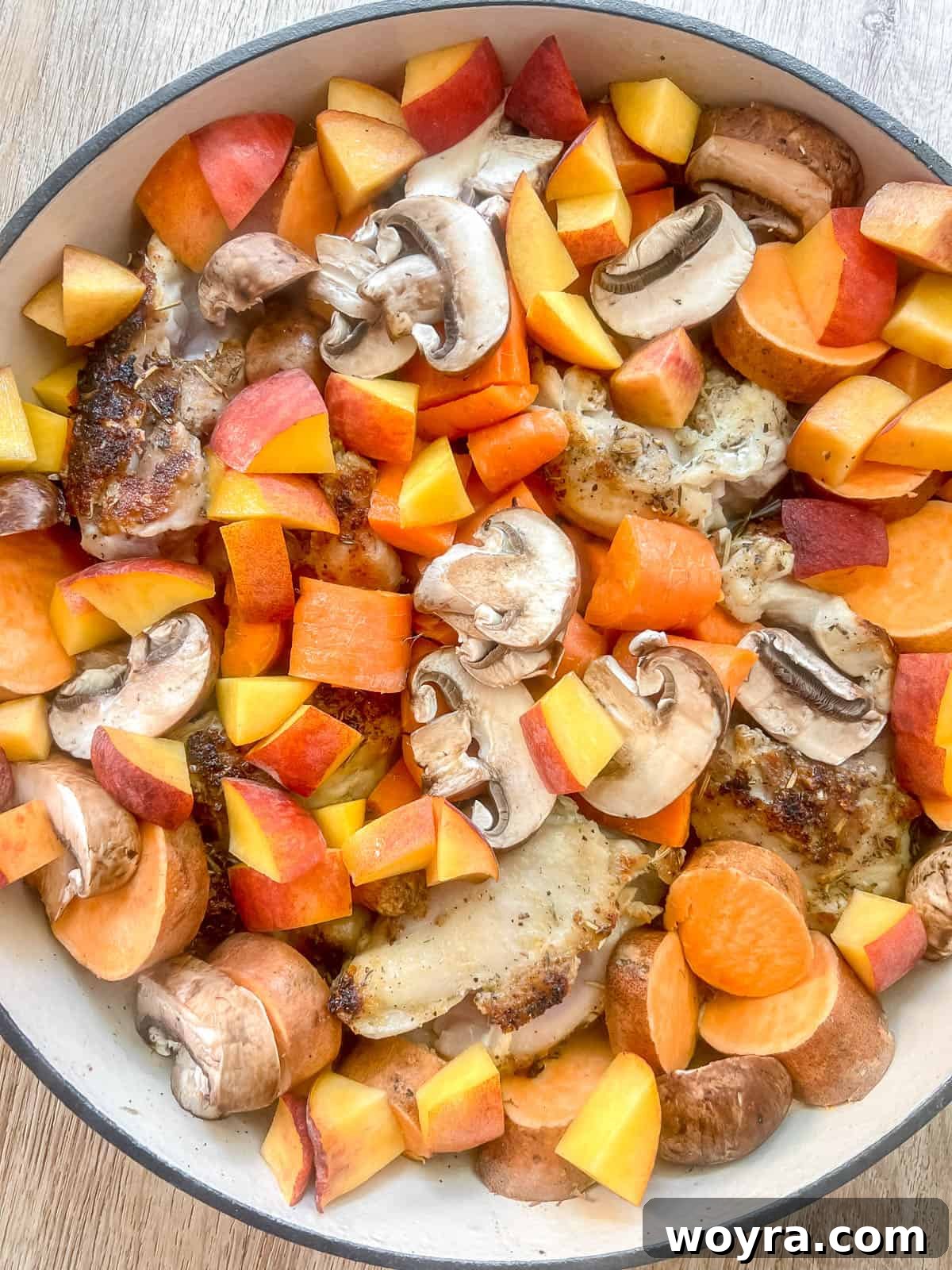 All the fresh ingredients, including peaches, mushrooms, carrots, and sweet potatoes, added around the seared chicken in the Dutch oven.