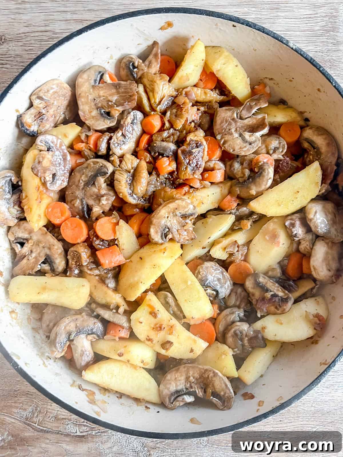 Dutch Oven Pork Tenderloin with Spiced Apples and Figs 6 Sliced apples, carrots, mushrooms, and figs added to a Dutch oven, mingling with aromatics. The ingredients are colorful and evenly distributed in the pan.