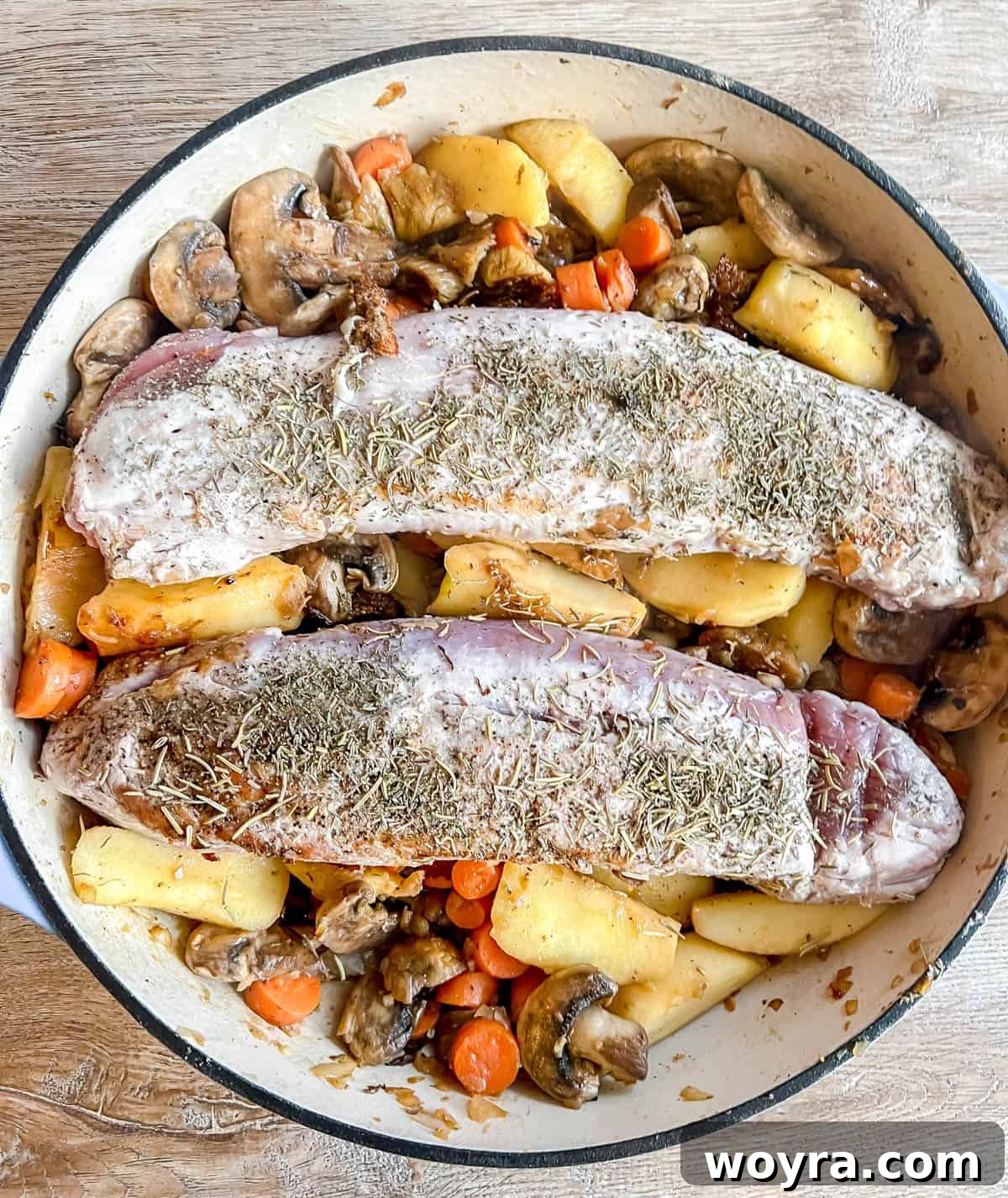 Dutch Oven Pork Tenderloin with Spiced Apples and Figs 7 Seared pork tenderloin returned to the Dutch oven, topped with fresh herbs, nestled among the cooked fruits and vegetables. The dish is arranged neatly before the final cooking stage.