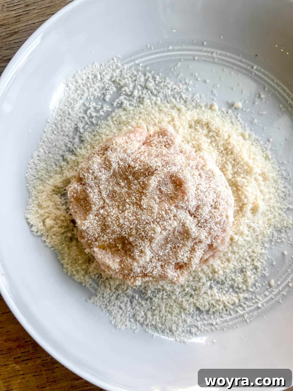 A chicken burger patty being coated in almond flour.