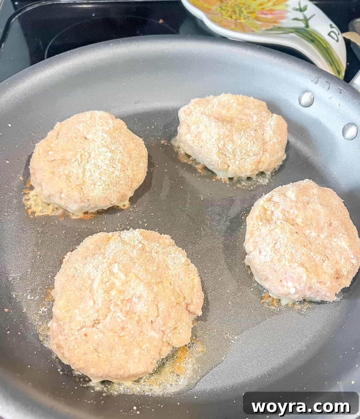 Chicken burgers sizzling in a hot frying pan.