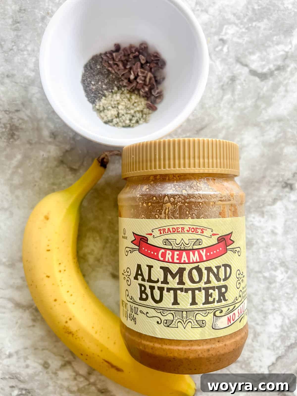 A collection of ingredients for banana sushi including bananas, almond butter, chia seeds, hemp hearts, and cacao nibs.