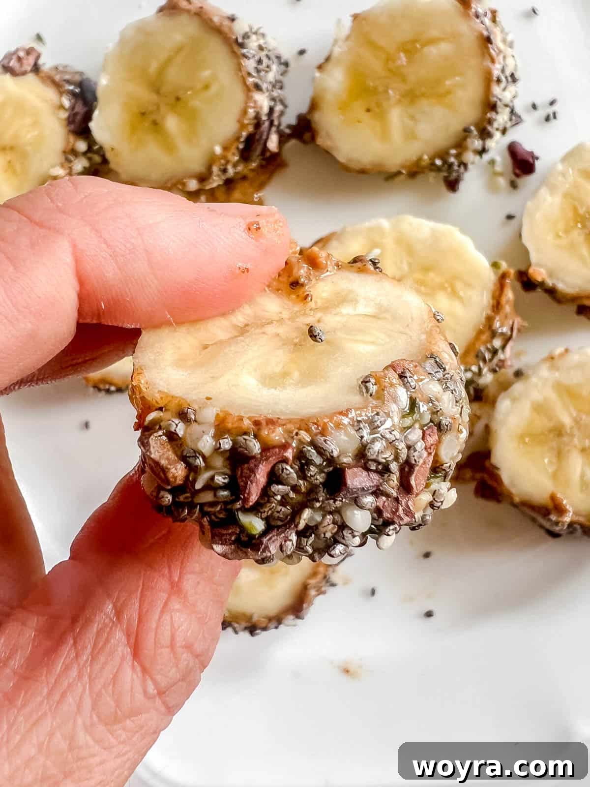 A hand holding a single slice of breakfast banana sushi, showcasing its layered toppings.