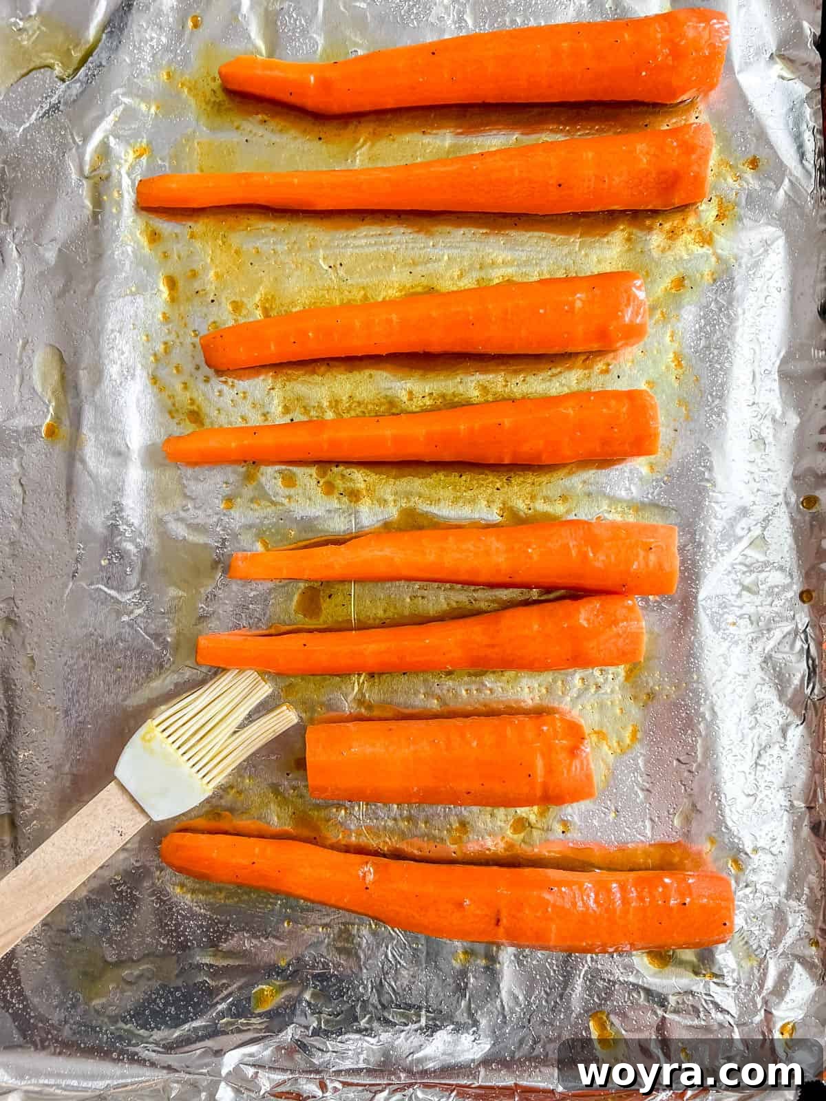 Carrots laid out on a greased baking sheet, ready to be coated with the maple turmeric sauce.