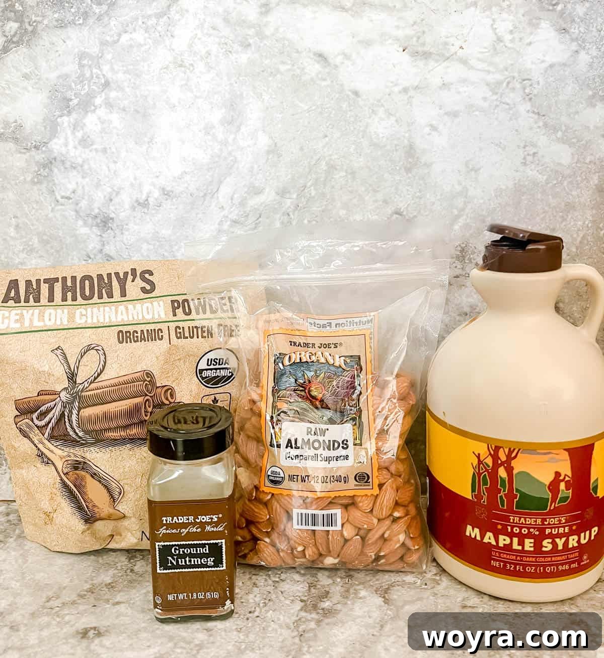 Warm Cinnamon Maple Roasted Almonds 3 A bowl of raw almonds, a bottle of maple syrup, ground cinnamon, and whole nutmeg displayed as ingredients for cinnamon maple roasted almonds.