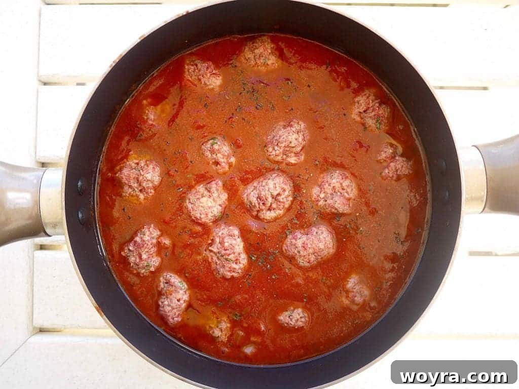 Savory Almond Flour Meatballs with Rich Sauce 7 Gluten-free meatballs being carefully placed into the simmering tomato sauce.