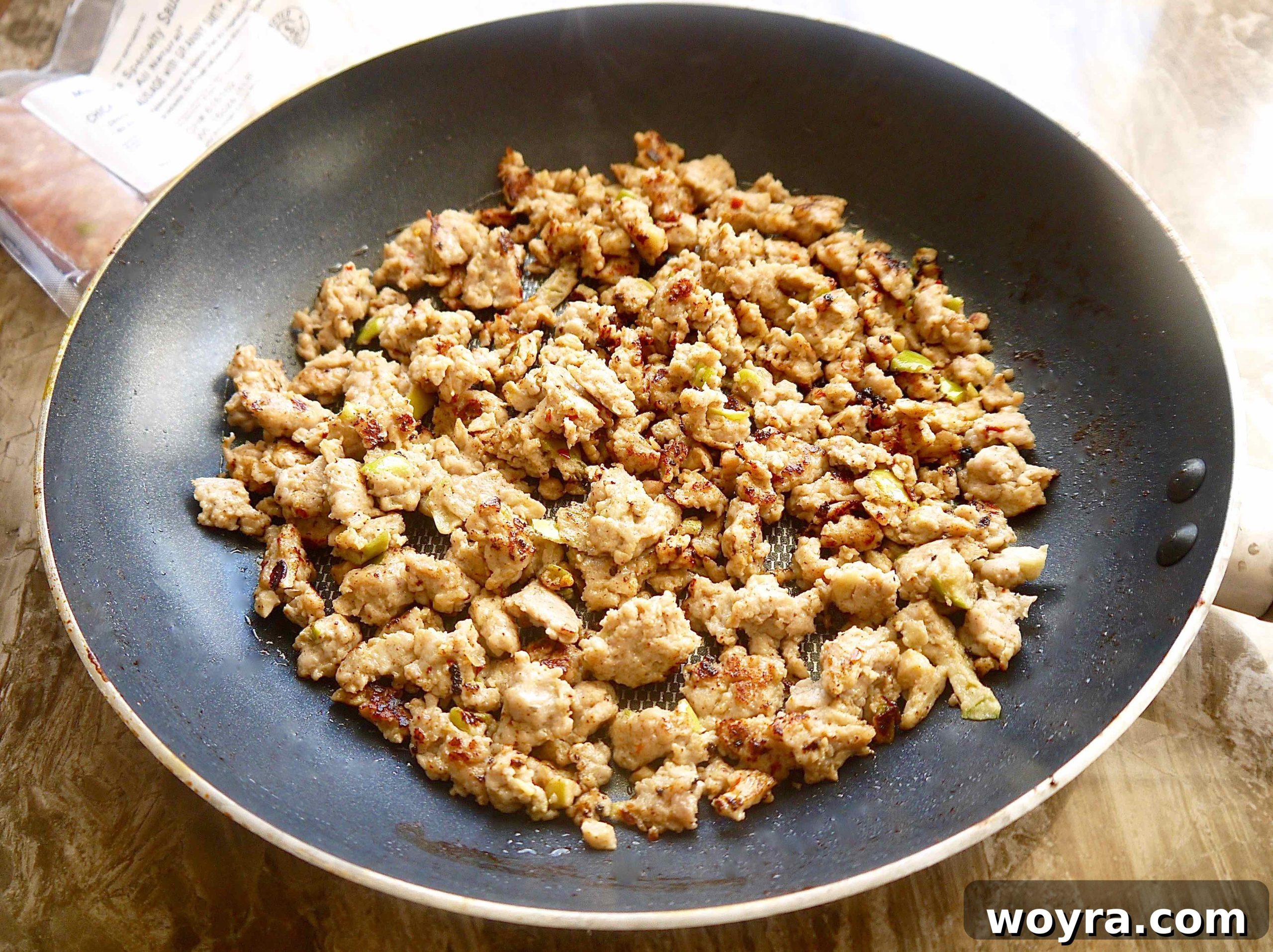 Crumbled and browned sausage cooking in a large skillet, ready to be transferred.