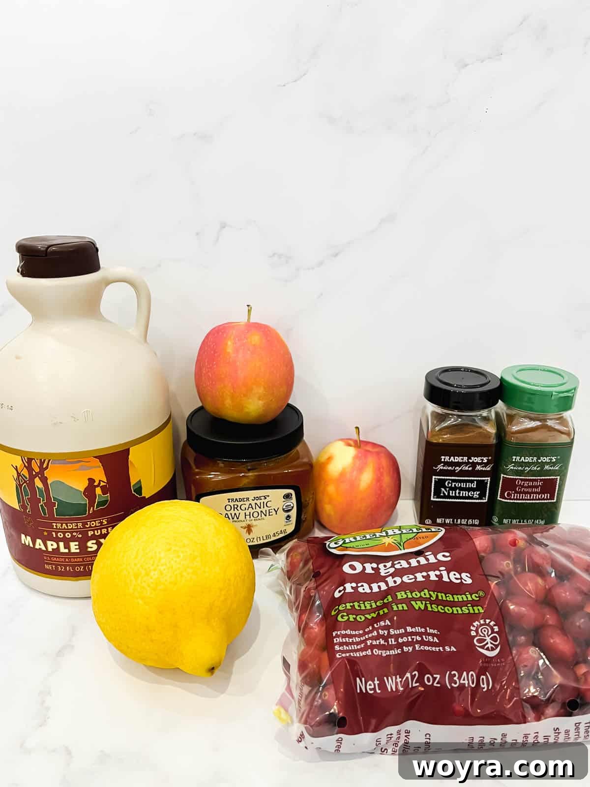 Homemade Cranberry Apple Sauce 3 Fresh cranberries, crisp apples, lemon, nutmeg, cinnamon, honey, and pure maple syrup carefully laid out on a clean wooden surface, showcasing their natural beauty and freshness, ready for making homemade cranberry apple sauce.
