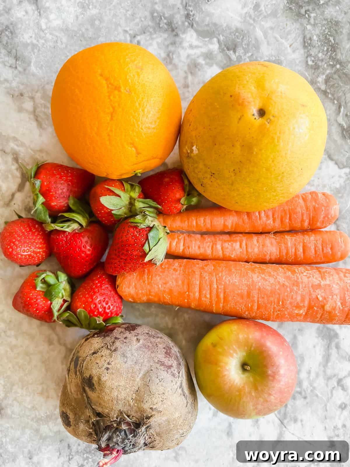 Red Root Berry Bliss 3 An array of fresh ingredients including grapefruit, oranges, carrots, strawberries, an apple, and a beet, ready for juicing.