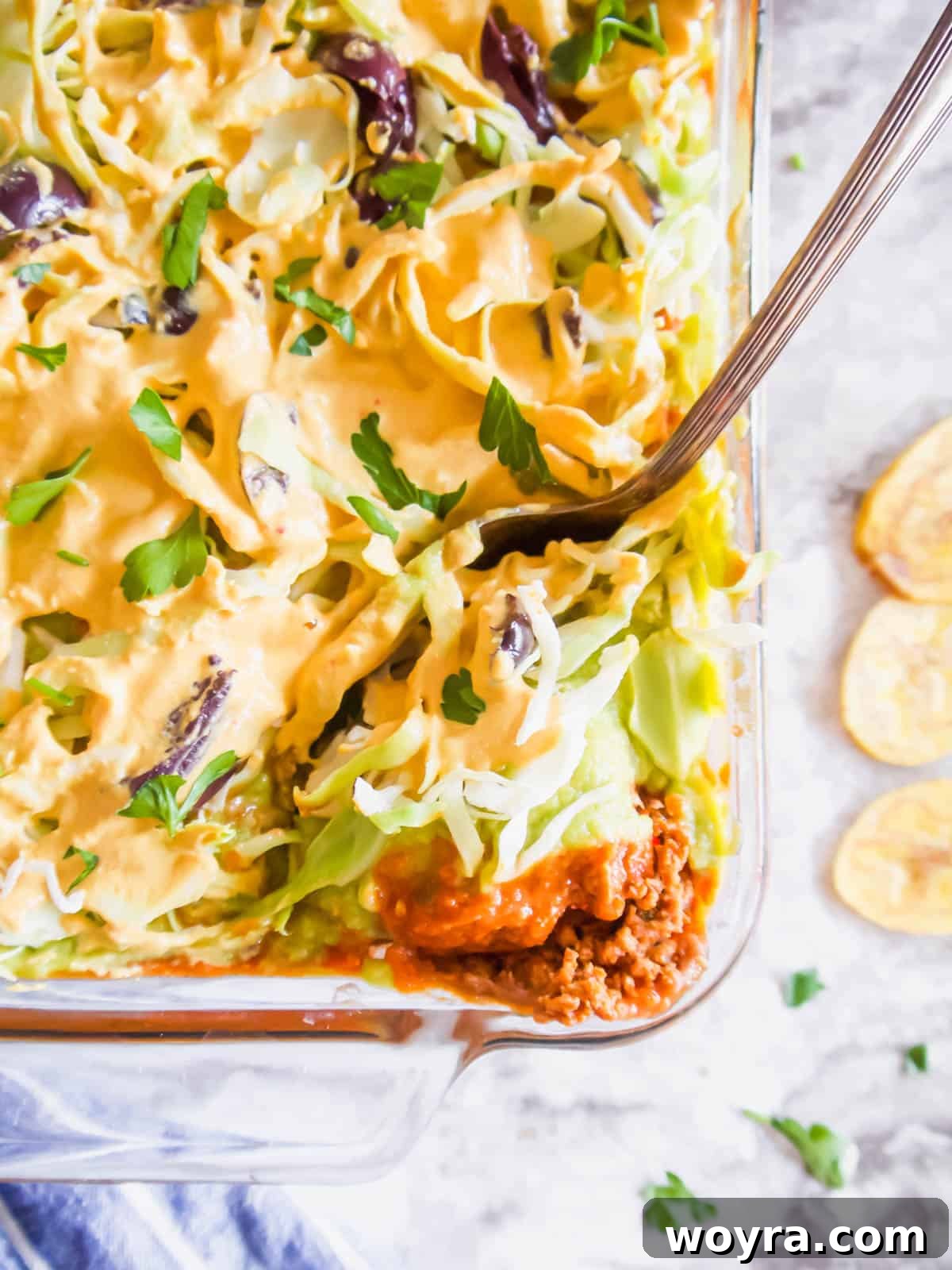 Ultimate Dairy-Free 7 Layer Turkey Taco Dip 2 Dairy free taco dip in a pan with a spoon inside of it, showcasing its delicious layers.